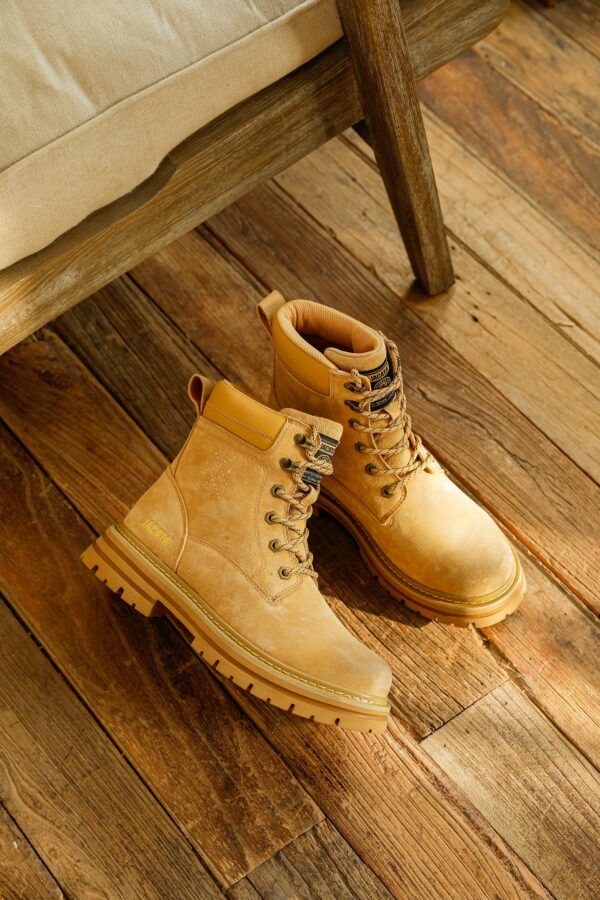 Stylish tan leather boots with laces on a rustic wooden floor, showcasing footwear design.