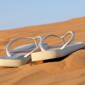 Pair of flip flops placed on sunlit desert sand, symbolizing a summer journey.