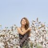 A carefree woman in a floral dress enjoying her time in a vibrant cotton field under a clear sky.