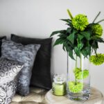 Sophisticated room decor featuring green flowers in a vase, soft pillows, and chic glass jar.