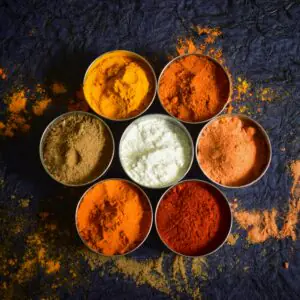 Colorful Indian spices in bowls on a textured dark background for culinary concepts.