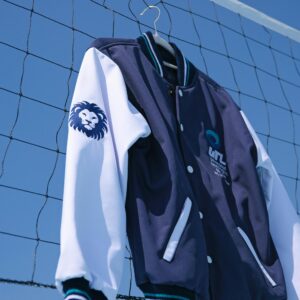 A stylish navy blue varsity jacket hangs on a net outside, featuring a lion emblem on the sleeve.